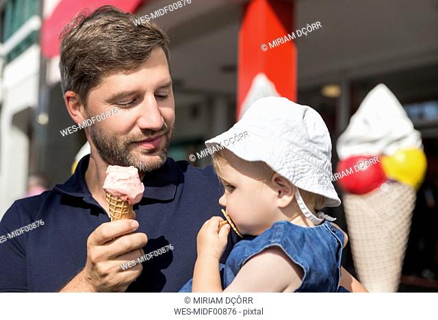 Father eating ice cream holding daughter