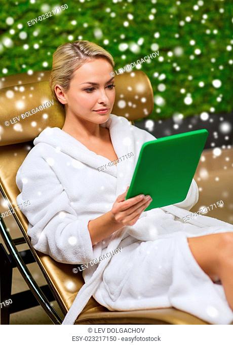 people, beauty, lifestyle, technology and relaxation concept - beautiful young woman in white bath robe with tablet pc computer social networking at spa with...