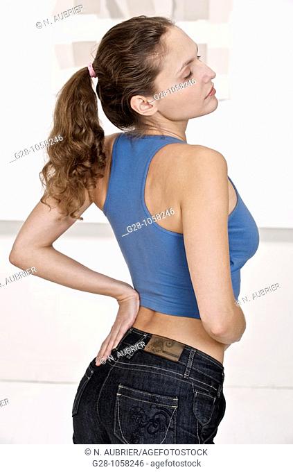 young woman in blue sports top, suffering from backache and holding her back with one hand
