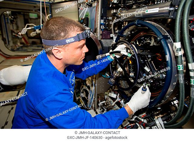 NASA astronaut Reid Wiseman, Expedition 40 flight engineer, performs routine in-flight maintenance on the Multi-user Drop Combustion Apparatus (MDCA) inside the...