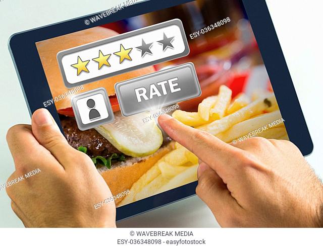 Hand touching tablet with Rate button and review stars in restaurant with burger dinner food