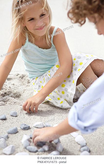 Siblings playing with pebbles on beach