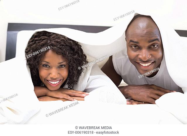 Happy couple lying on bed together under the duvet