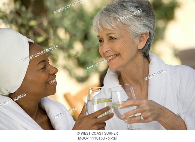 Two women in bathrobes toasting drinks