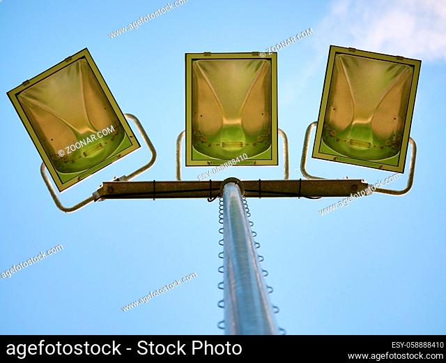 Tall steel lamp in the park on blue sky in background. High stadium light, spot light pole