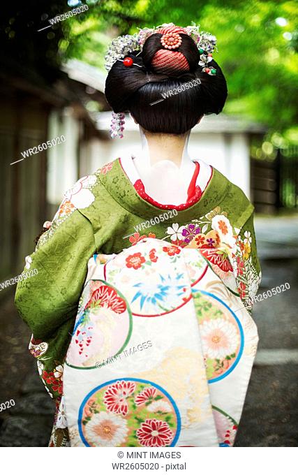 A woman dressed in the traditional geisha style, wearing a kimono and obi, with an elaborate hairstyle and floral hair clips