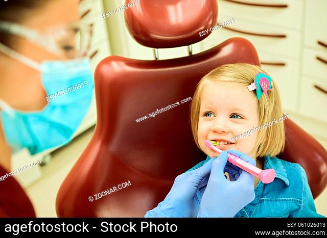 Little girl sitting in the dentists office. The dentist brushes teeth to the little girl