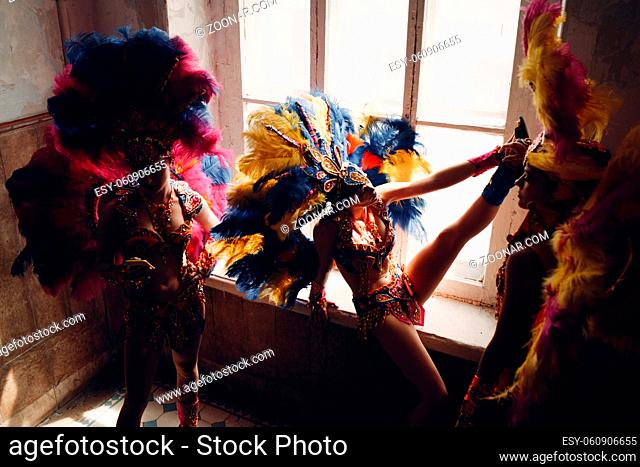 Woman in brazilian samba carnival costume with colorful feathers plumage relax in old entrance with big window