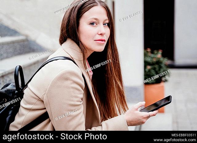 Young woman with backpack staring while holding smart phone