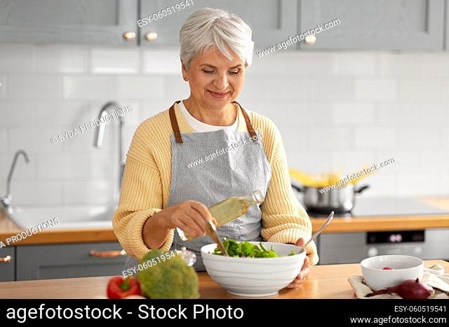 happy woman adding cooking oil to salad on kitchen