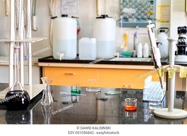 Pipette and colourful chemical liquid solutions in flasks on laboratory worktop, lab equipment and glassware in background