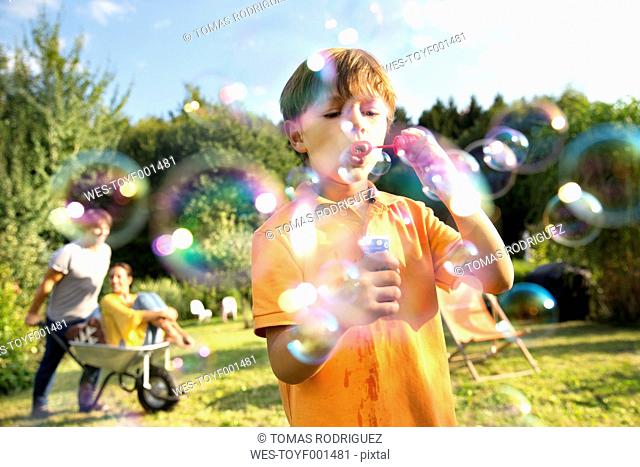 Happy family in garden with man pushing woman in wheelbarrow and boy blowing soap bubbles