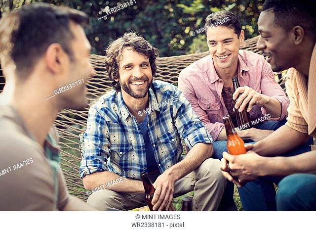 A group of friends lounging in a large hammock in the garden having a beer