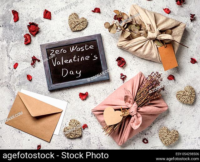 Zero waste Valentine's Day concept. Eco-friendly gift cloth wrapping in Furoshiki style and chalkboard with Zero Waste Valentine's Day letters on gray textured...