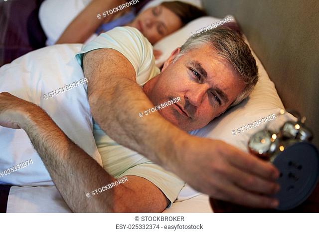 Couple In Bed With Man Reaching To Switch Off Alarm Clock