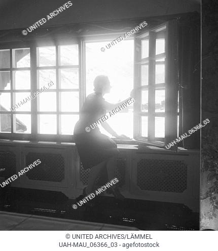 Eine junge Frau blick aus dem Fenster eines Hotels in Zürs am Arlberg, Deutsches Reich 1930er Jahre. A young woman at the window of a hotel with view to...