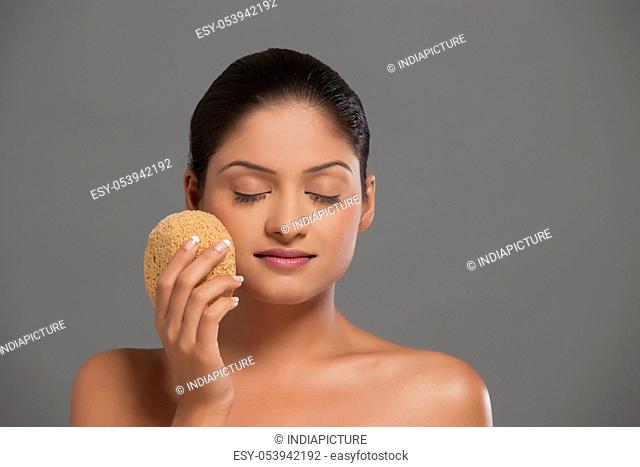 Close-up of young woman using massage sponge over grey background