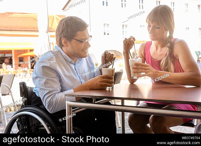 Two friends in a cafe drinking coffee in summer, the man sitting in wheelchair