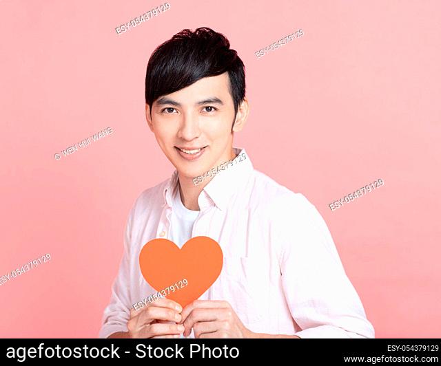 Happy young man holding red paper hearts and celebrating valentines day