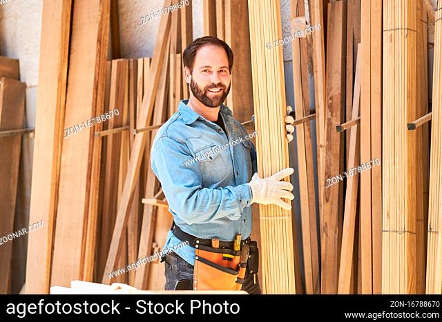 Junger Handwerker als Schreiner Lehrling trägt Bretter im Holzlager der Tischlerei