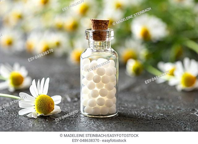 A bottle of homeopathic remedies with fresh chamomile flowers