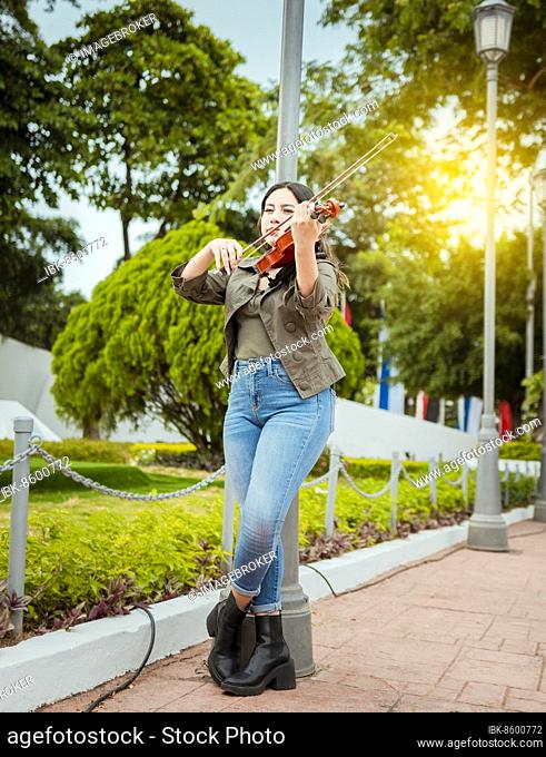 Woman playing violin in the street. Portrait of violinist girl playing in the street. Woman artist playing violin outdoors