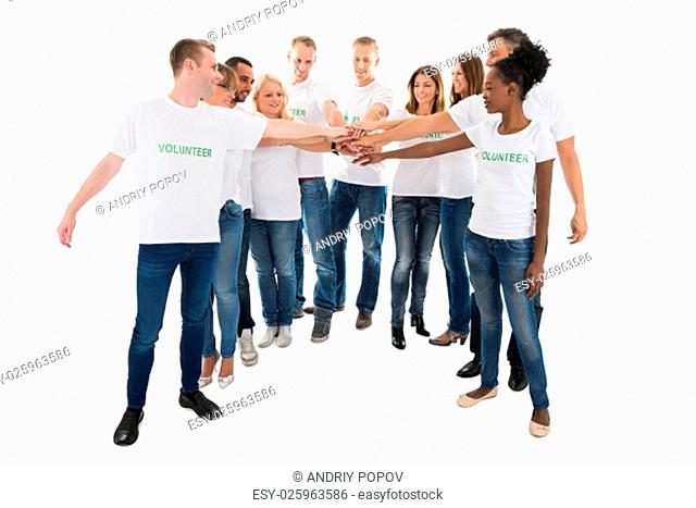 Full length of multiethnic volunteers stacking hands while standing against white background