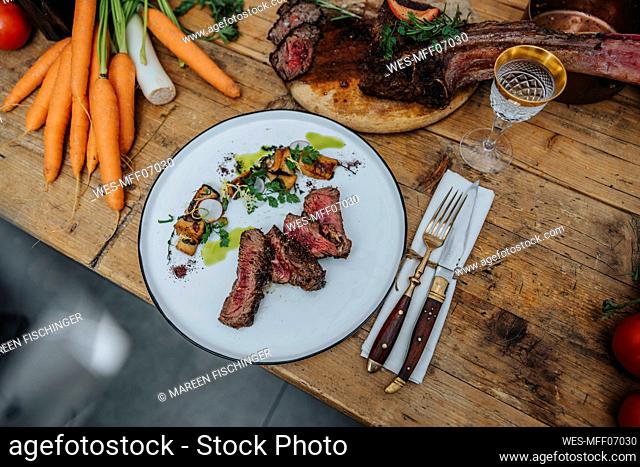 Tomahawk steak garnished with cooked vegetable in plate on kitchen island