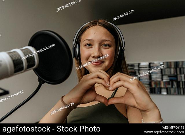 Close-up of smiling teenage girl making heart shape while singing in recording studio