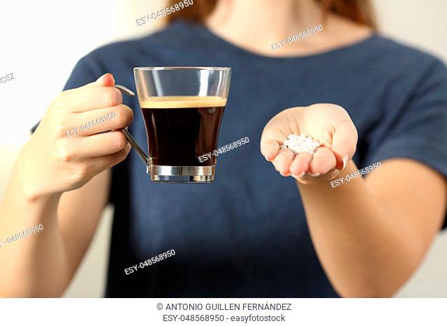 Front view close up of a woman hands holding a coffee cup and saccharin pills