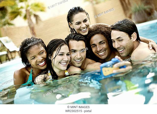 A group of young men and women in the swimming pool at the end of a hot day, posing for a selfy