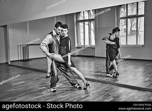 beautiful couple dancing tango. young woman in red dress and man in suit practicing in dancing studio mirror room. copy space