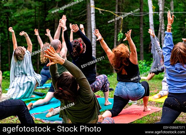A group of people of all age groups are seen in warrior I pose (virabhadrasana I), during an outdoor yoga session as part of a multicultural celebration