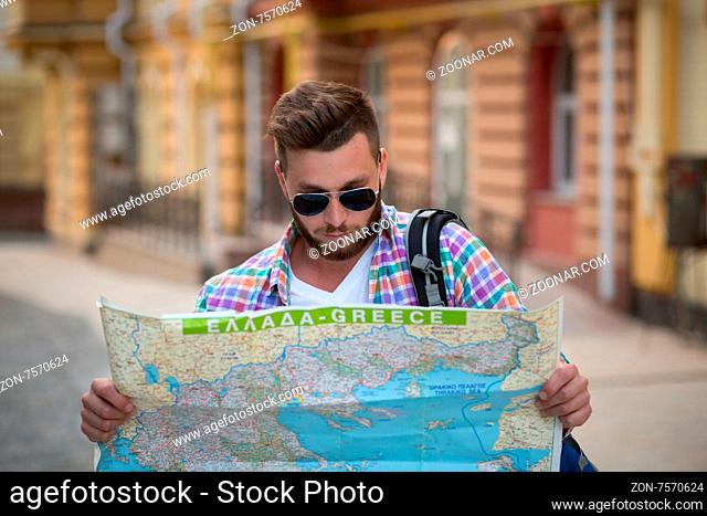 Young hipster man with map outdoors. Serious man with backpack going to find interesting sightseeings in the city