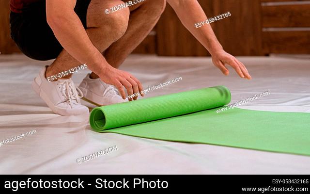 Fitness trainer young man, an athlete, unwinds a roll mat, preparing a place for sports. Determined guy doing physical training