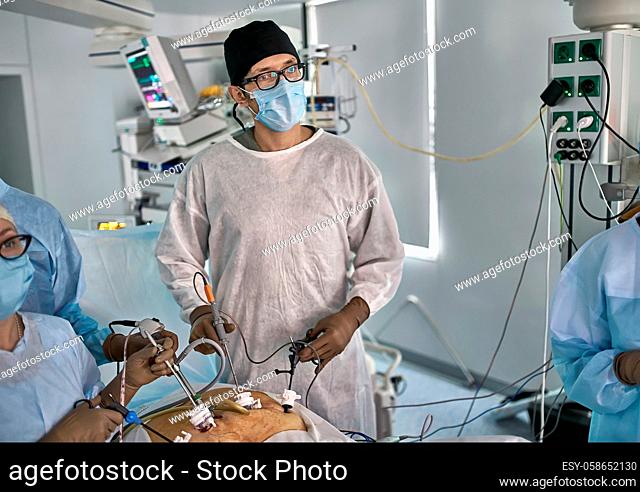 Surgeon with assistants are using laparoscopy cameras inside the patient's abdominal during the operation. There are medical equipment with an EKG monitor...