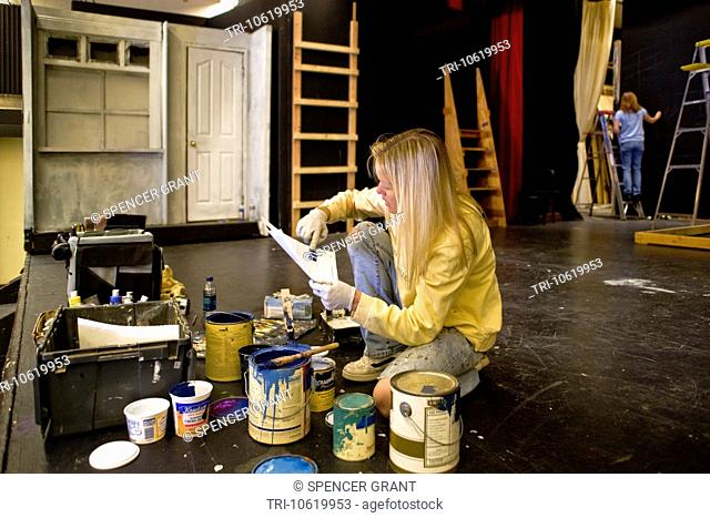 A high school student studies paint color samples while building the set of a play in her school's theatre. Stagecraft is an elective course at the school