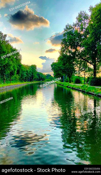Beautiful and dramatic sunset or sunrise with colorful clouds and light rays in the sky over the river or canal with reflections on the water
