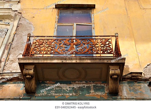 Winged female figure rusty floral pattern and swans on balcony balustrade of abandoned neoclassical house. Athens Greece