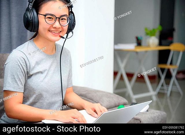 Asian young woman student with headphones sitting on the sofa smile looking up happy study online class college learning internet education