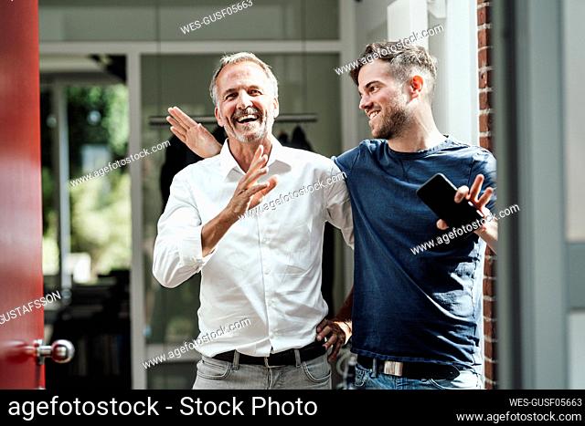 Son with smart phone looking at smiling father gesturing during sunny day