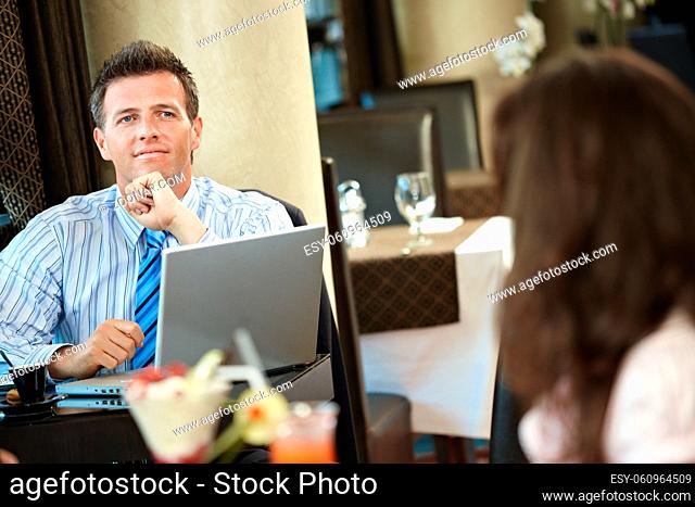 Businessman sitting at table in cafe using laptop computer, thinking