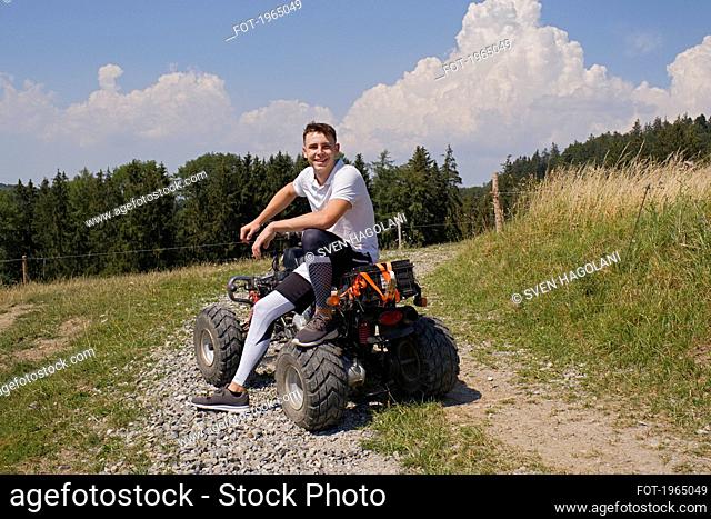 Portrait happy teenage boy on quadbike on sunny rural gravel road