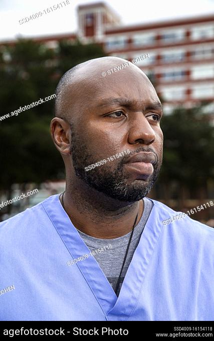 Portrait of middle aged man with beard and a bald head wearing scrubs standing outside looking off camera
