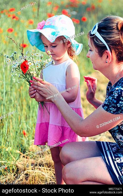 Mother and her little daughter in the field of wild flowers. Little girl picking the spring flowers for her mom for Mother's Day in the meadow
