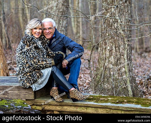 A 60 Year old blond woman and a 66 year old man enjoying each other's company on a chilly day in a forest setting