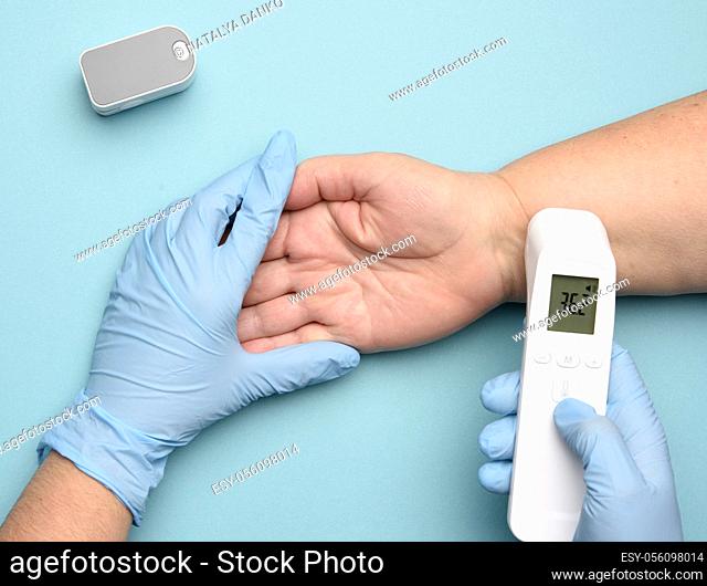 doctor in blue latex gloves measures the temperature with an electronic contactless gadget on a woman's hand, blue background