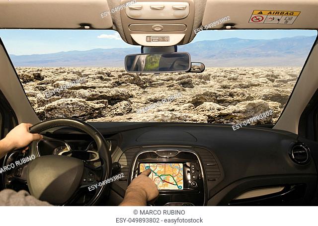 Driving a car while using the touch screen of a GPS navigation system towards Devil's Golf Course, Death Valley, USA