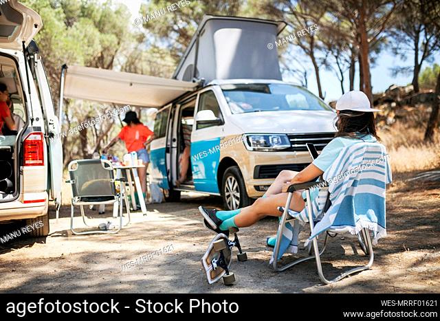 Woman with feet up sitting on chair by camper van