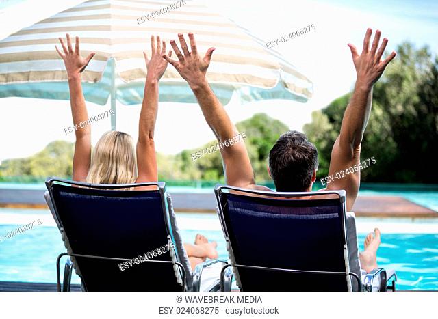 Rear view of couple relaxing on sun lounger with hand raised